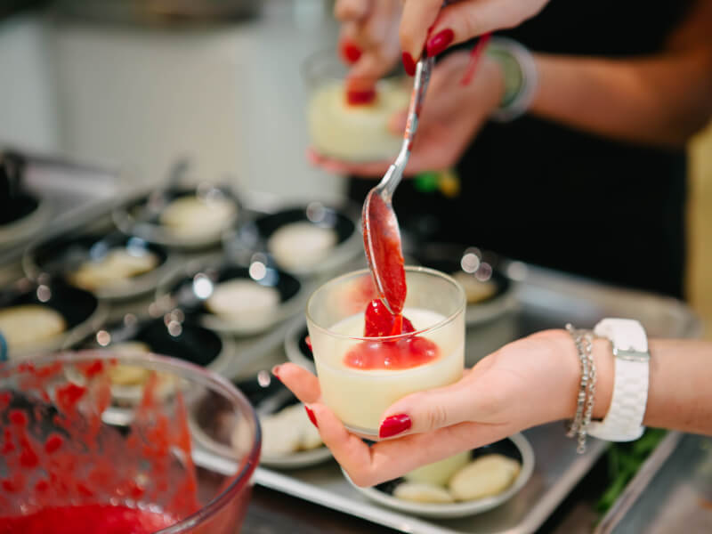 Woman spooning berry compote onto panna cotta